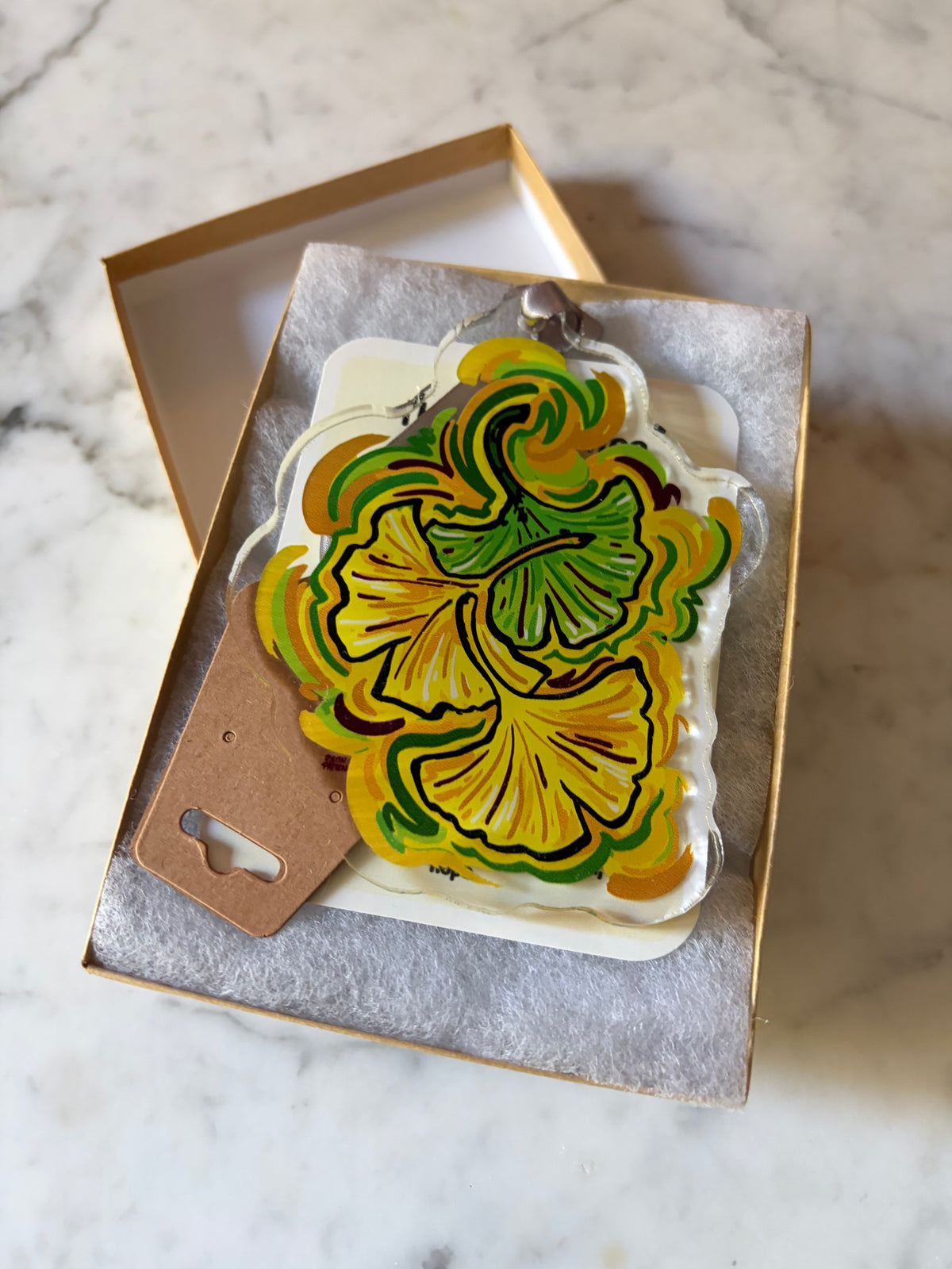 Ginkgo leaf acrylic ornament in open gray gift box with brown hanging tag