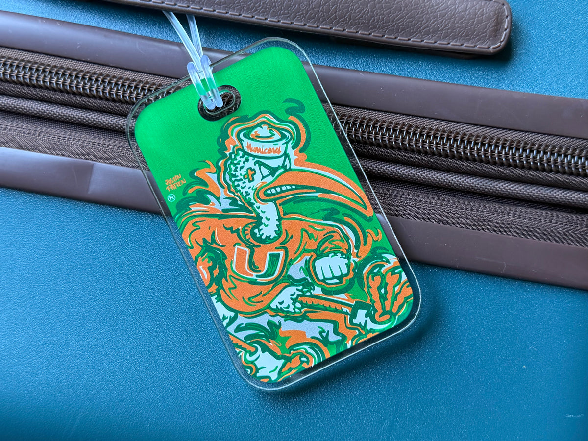 Green mascot bag tag with orange and teal U graphic, clipped to luggage zipper.