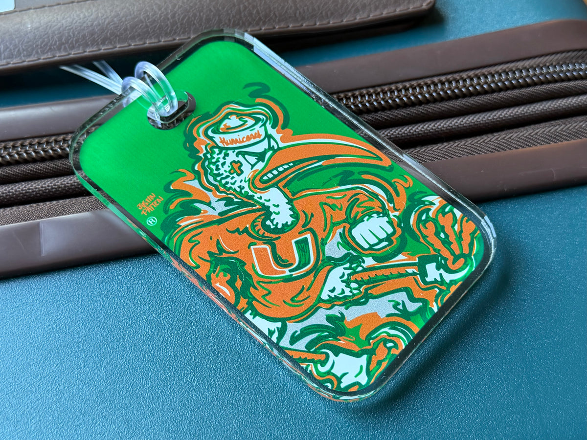 Green mascot bag tag with orange-and-teal University graphic on luggage zipper.