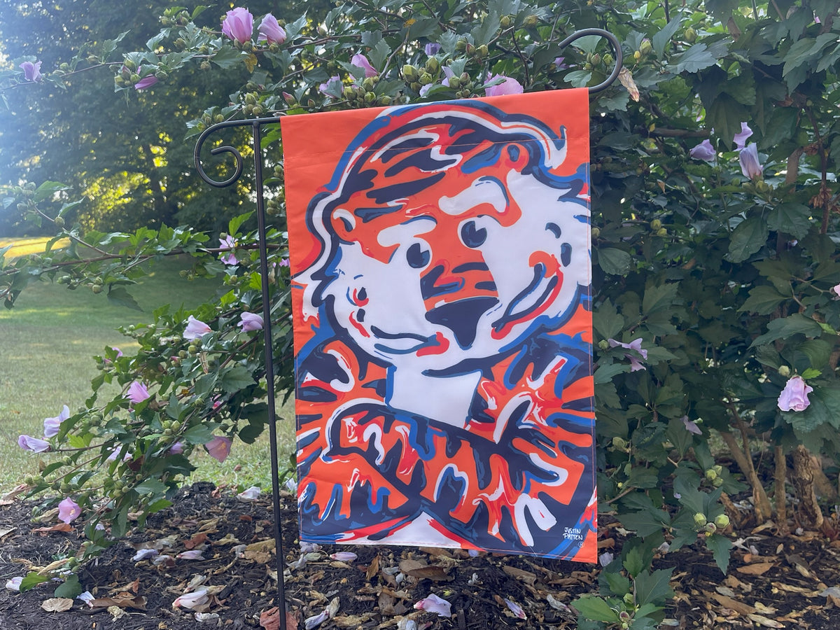 Auburn Aubie 12x18 garden flag in a yard, orange background and blue dog graphic
