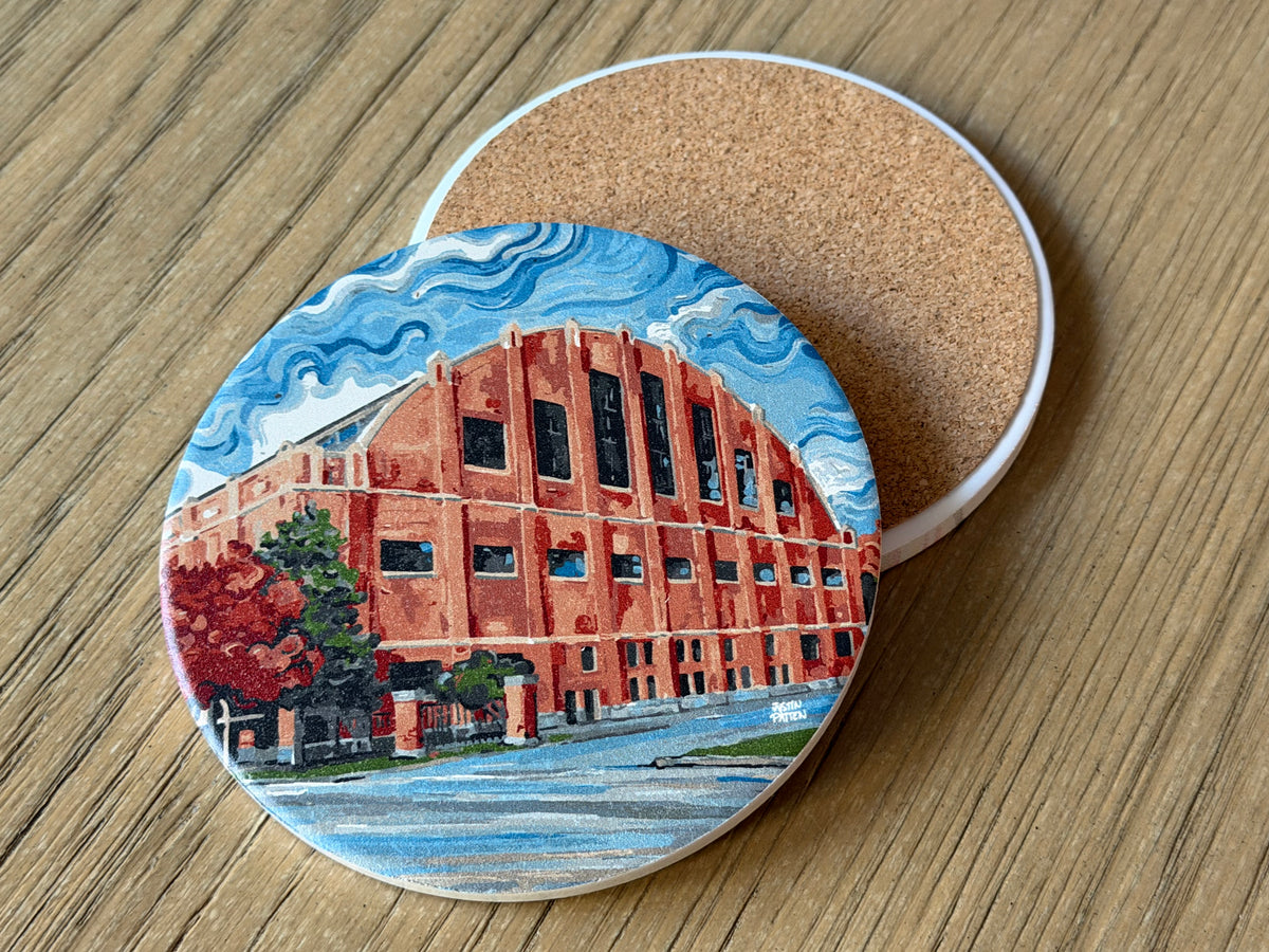 Round cork-backed stone coaster with red building art and blue sky design