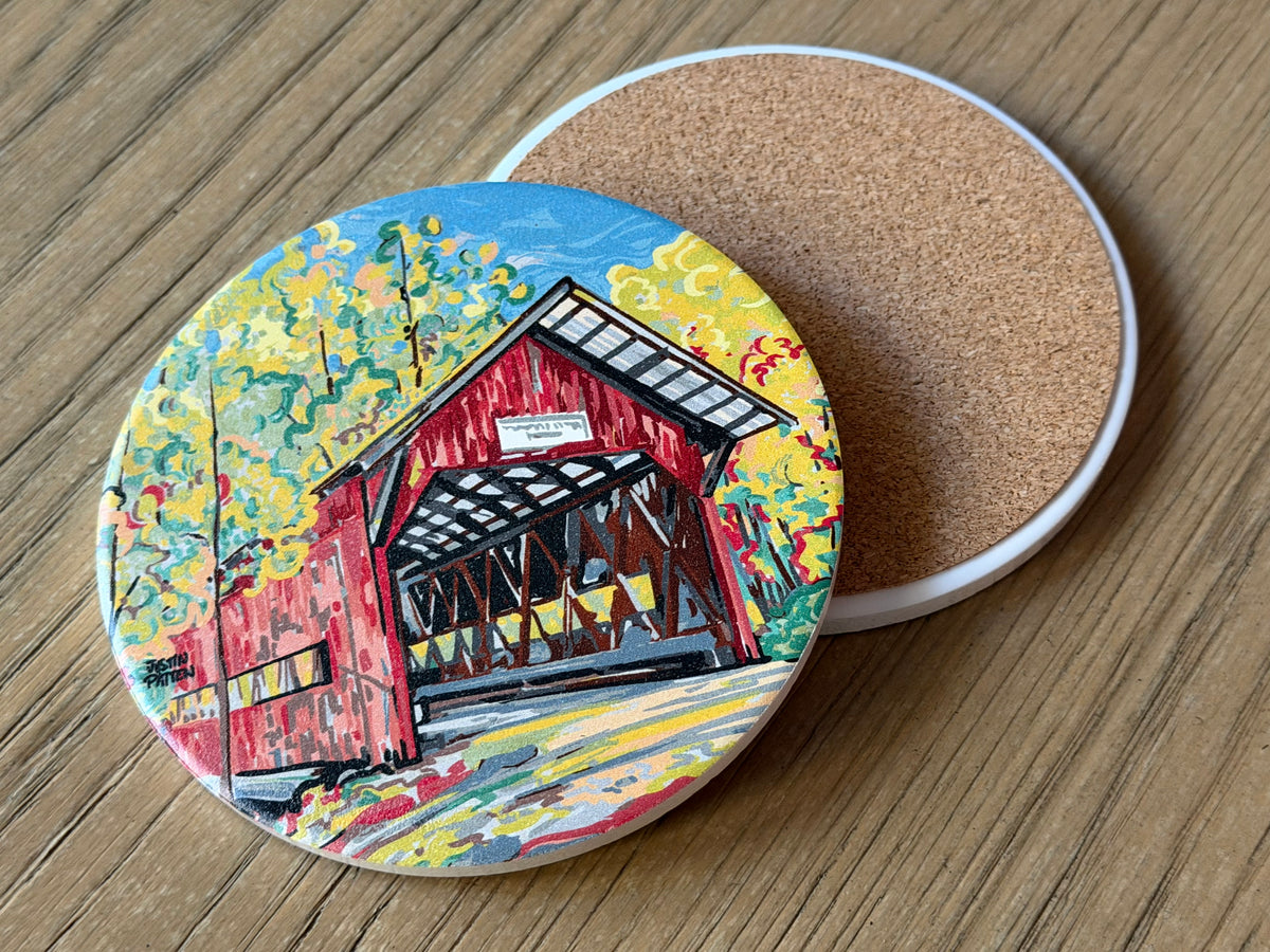 Round stone coaster with colorful covered bridge artwork; cork backing visible