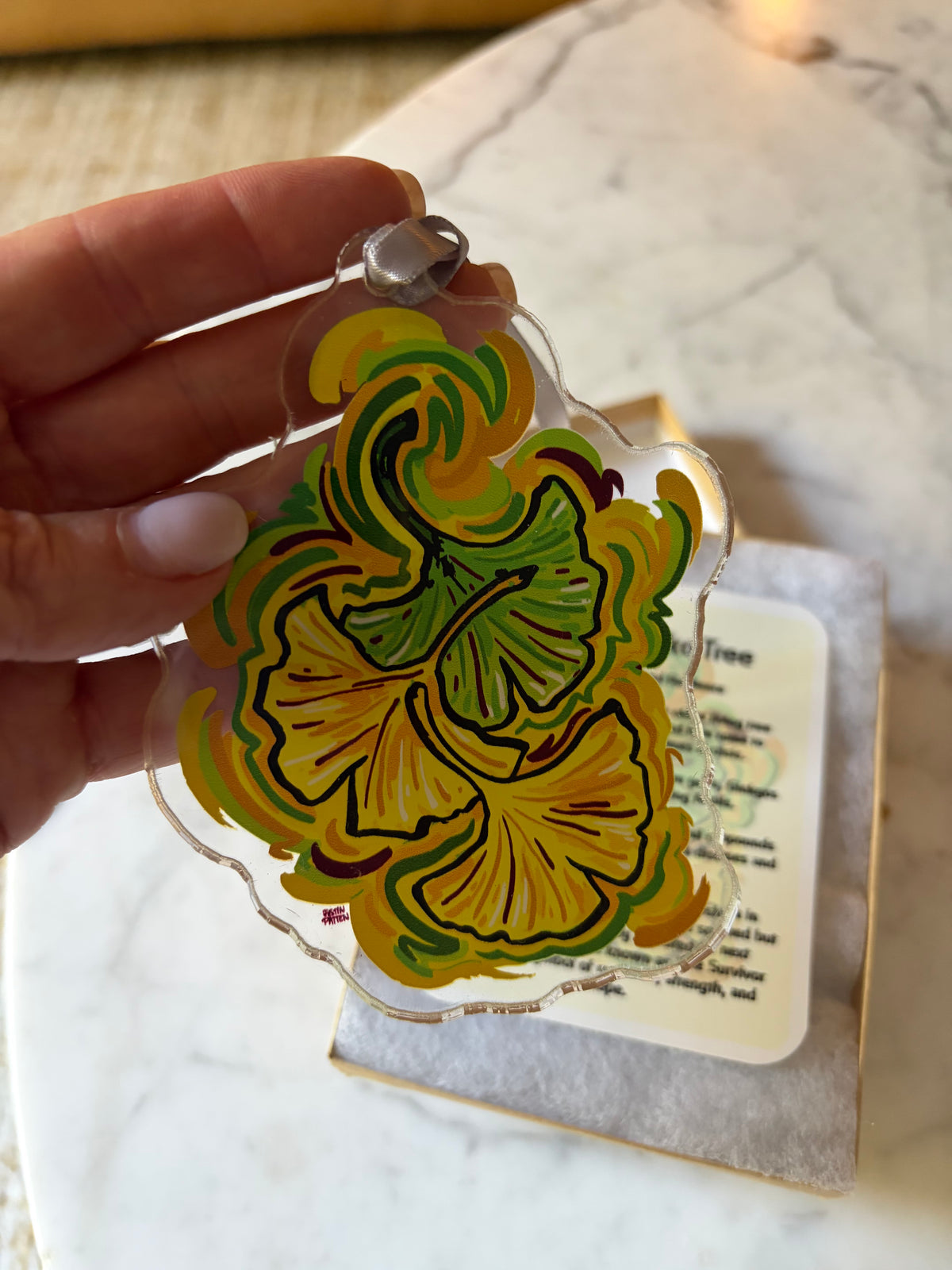Ginkgo leaf acrylic ornament with metal loop, held in hand over a gift card