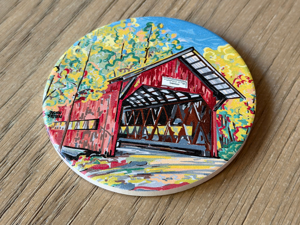Round stone coaster featuring a red covered bridge with yellow trees