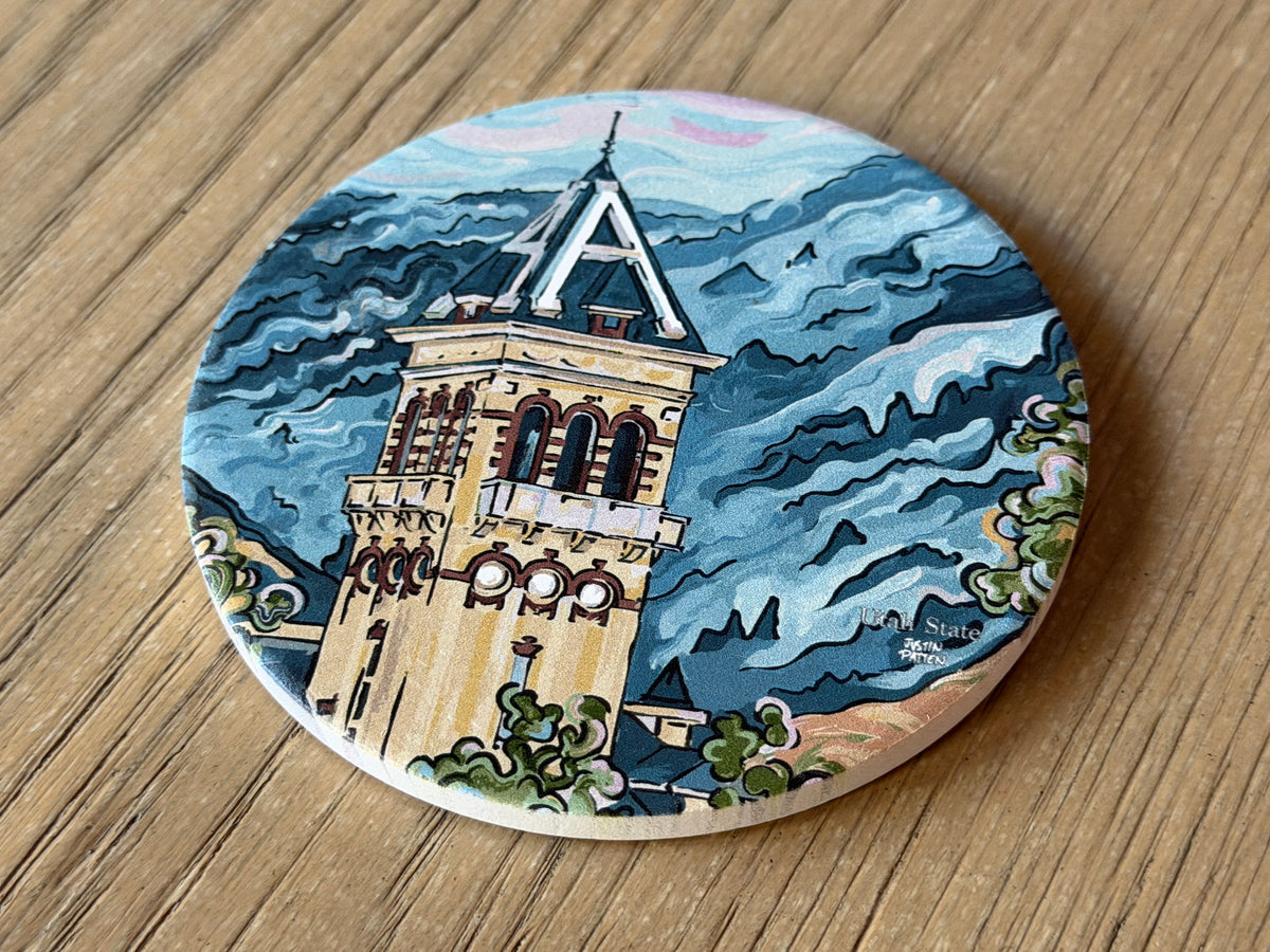 Round stone coaster with illustrated campus building, blue sky and wave patterns