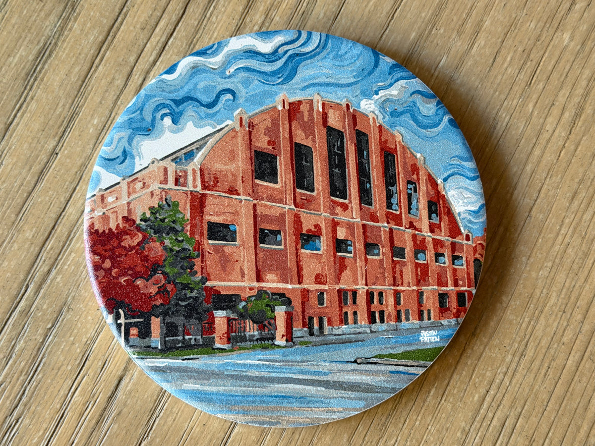 Round stone coaster with red brick building illustration and blue water and sky