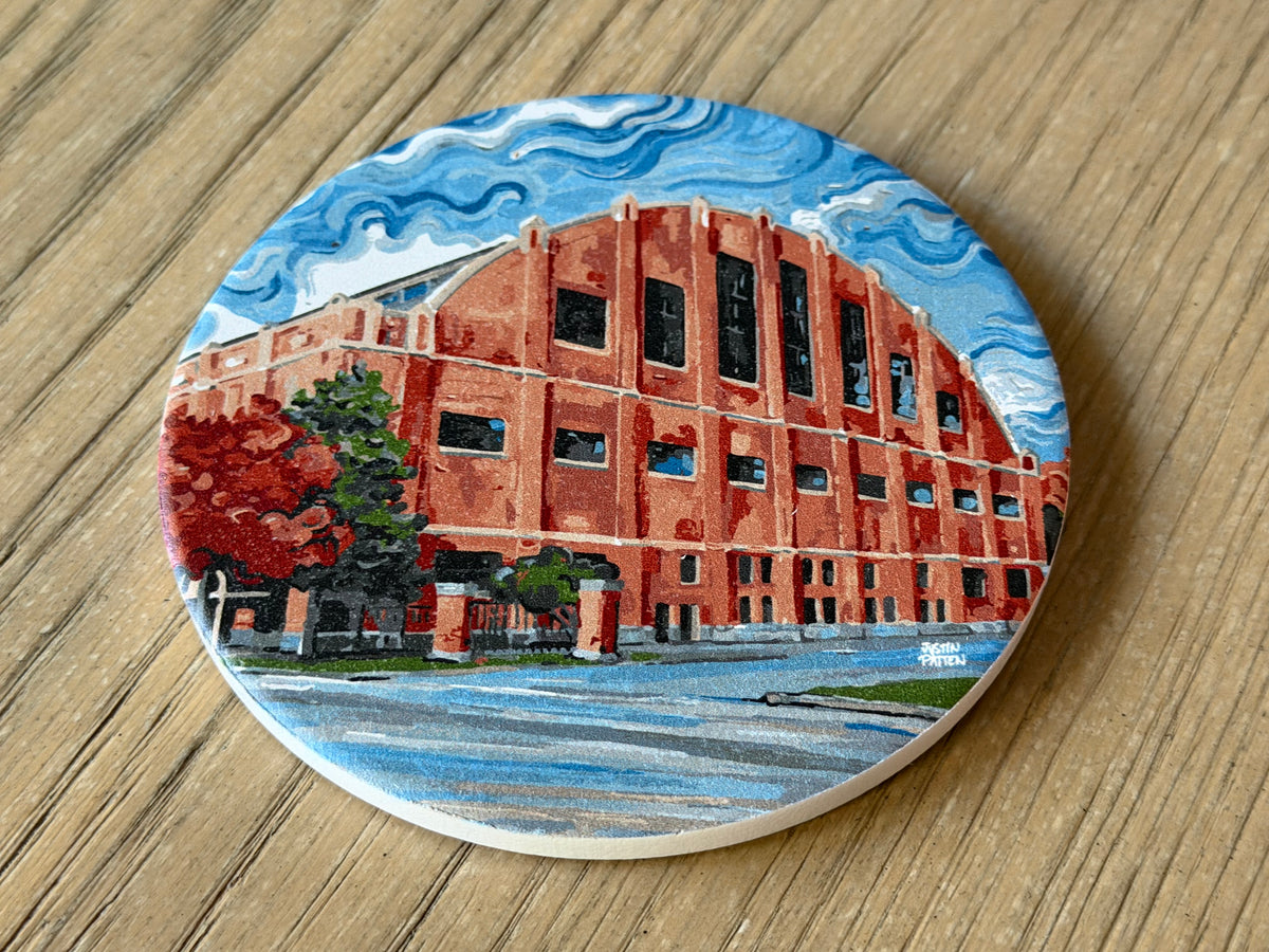 Round stone coaster showing red building, trees, and blue wave-like sky