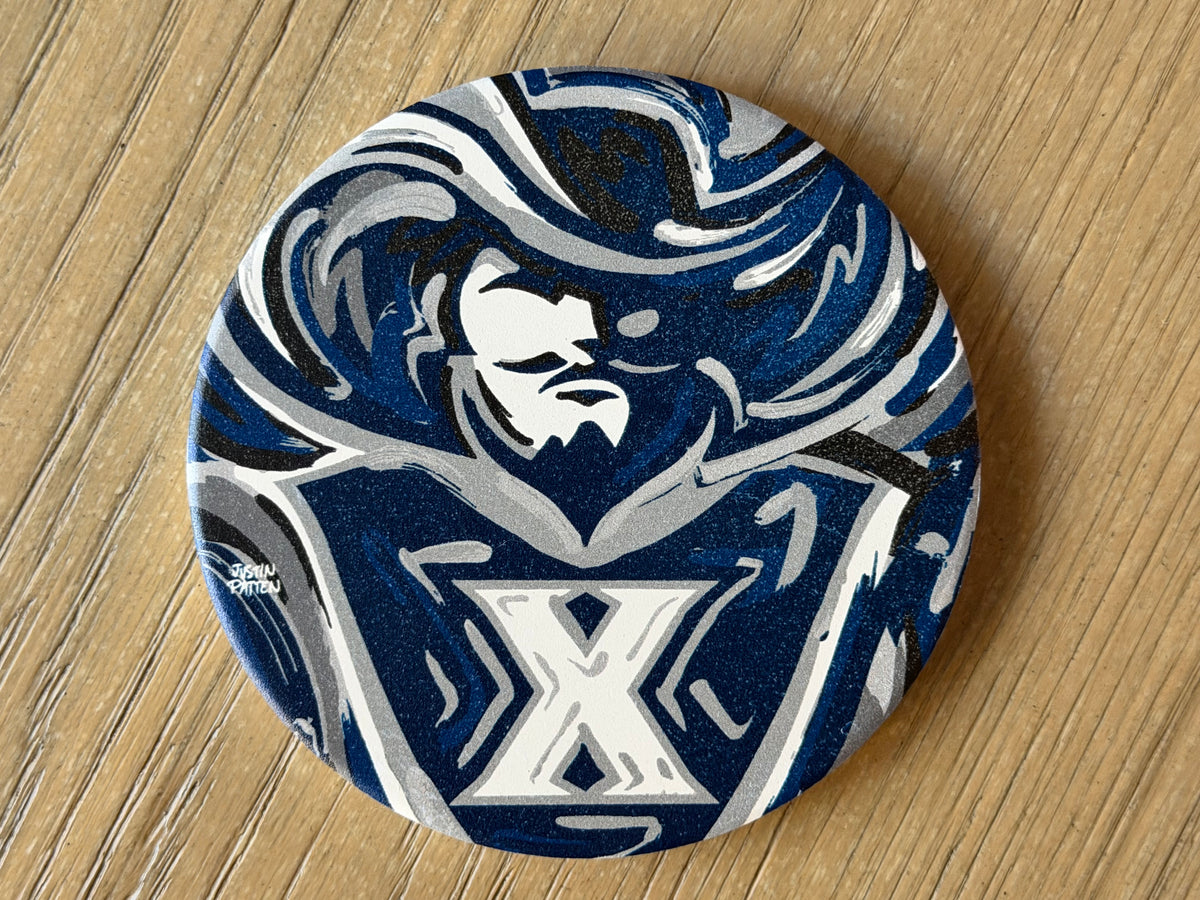 Round coaster top with blue and white mascot face and X logo