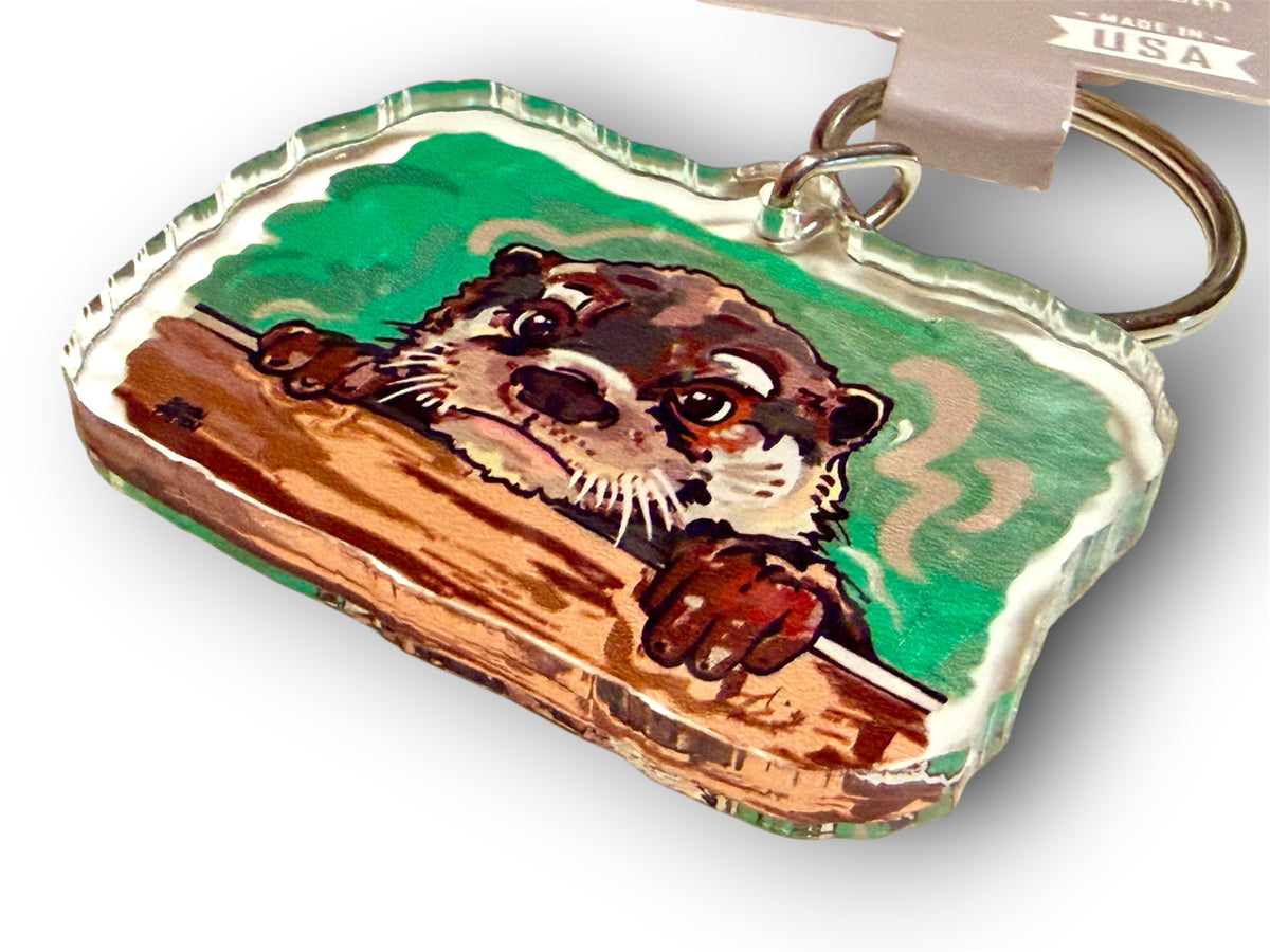 Otter keychain with stitched-edge fabric tag, cartoon otter on log with green waves